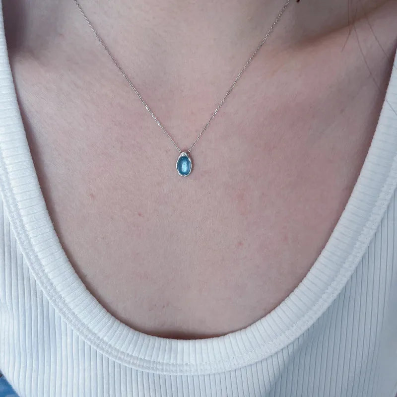 Close-up of a navy blue geometric water drop pendant on an adjustable silver-tone cross chain necklace.