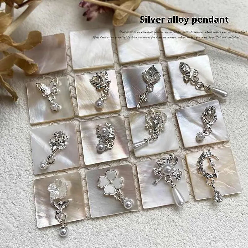 Silver nail art pendant charms with pearl and tassel details, assorted pack on black background