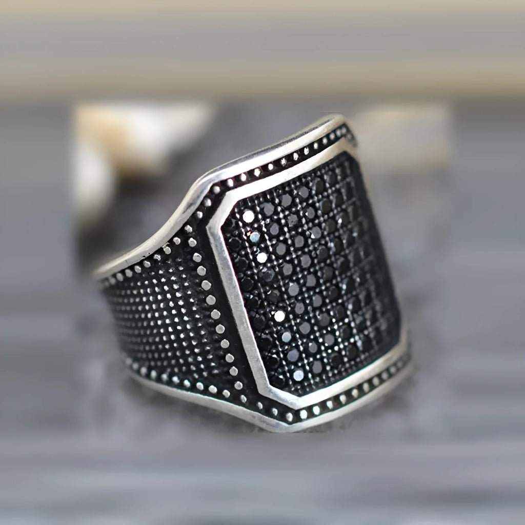 A black alloy ring on a finger, showing a copper metal inlay and sparkling clear zircon stones set into the band.