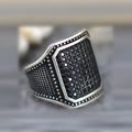 A black alloy ring on a finger, showing a copper metal inlay and sparkling clear zircon stones set into the band.
