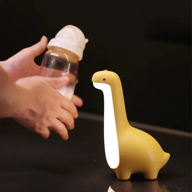 Dinosaur night light in lemon yellow with warm 3000K glow on a bedside table, USB charging cable included