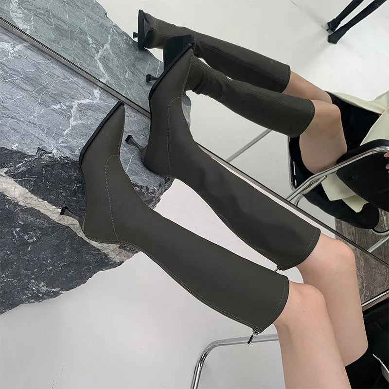 Black pointed-toe below-knee women's boots with a stiletto heel and a visible back zip on a neutral background.