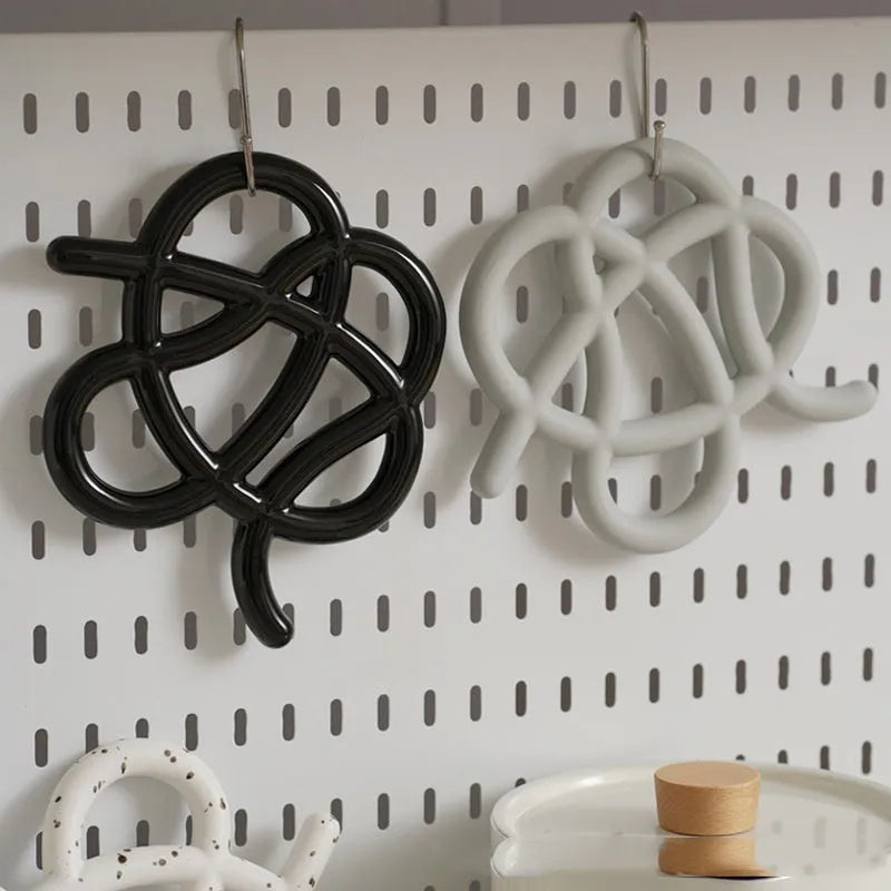 Irregular-shaped ceramic heat proof mat in grey on a wooden table next to a hot pan.