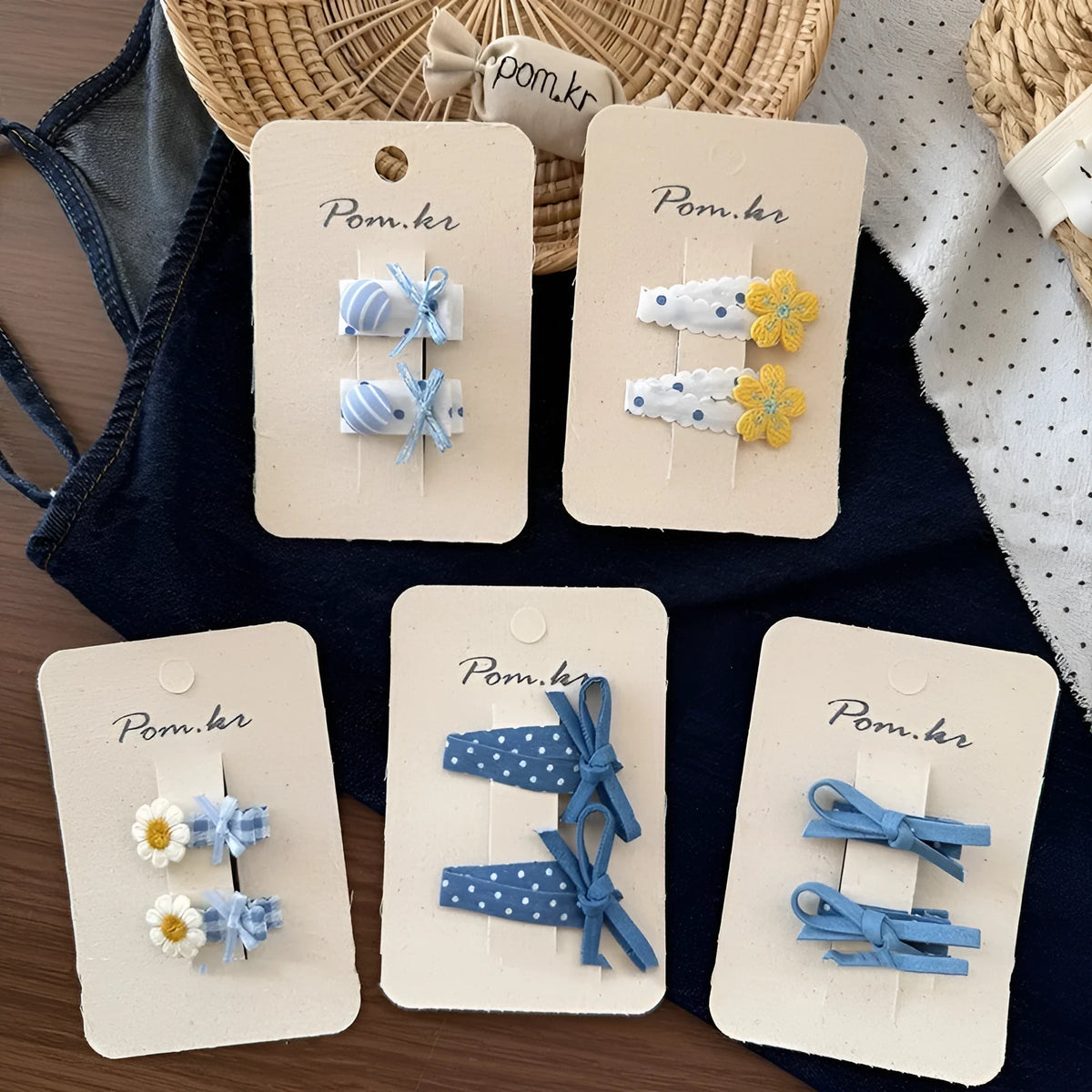 One pair of children's cloth hair clips with bow and flower detailing, shown in a choice of five styles and two clip sizes.