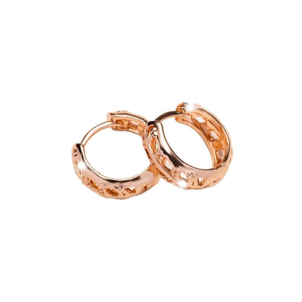 Close-up of rose gold plated copper stud earrings with hollow leaf and heart shapes on a grey background.