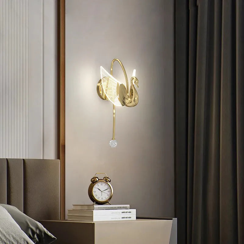 Gold modern swan-shaped wall lamp with acrylic shade mounted beside a bed.