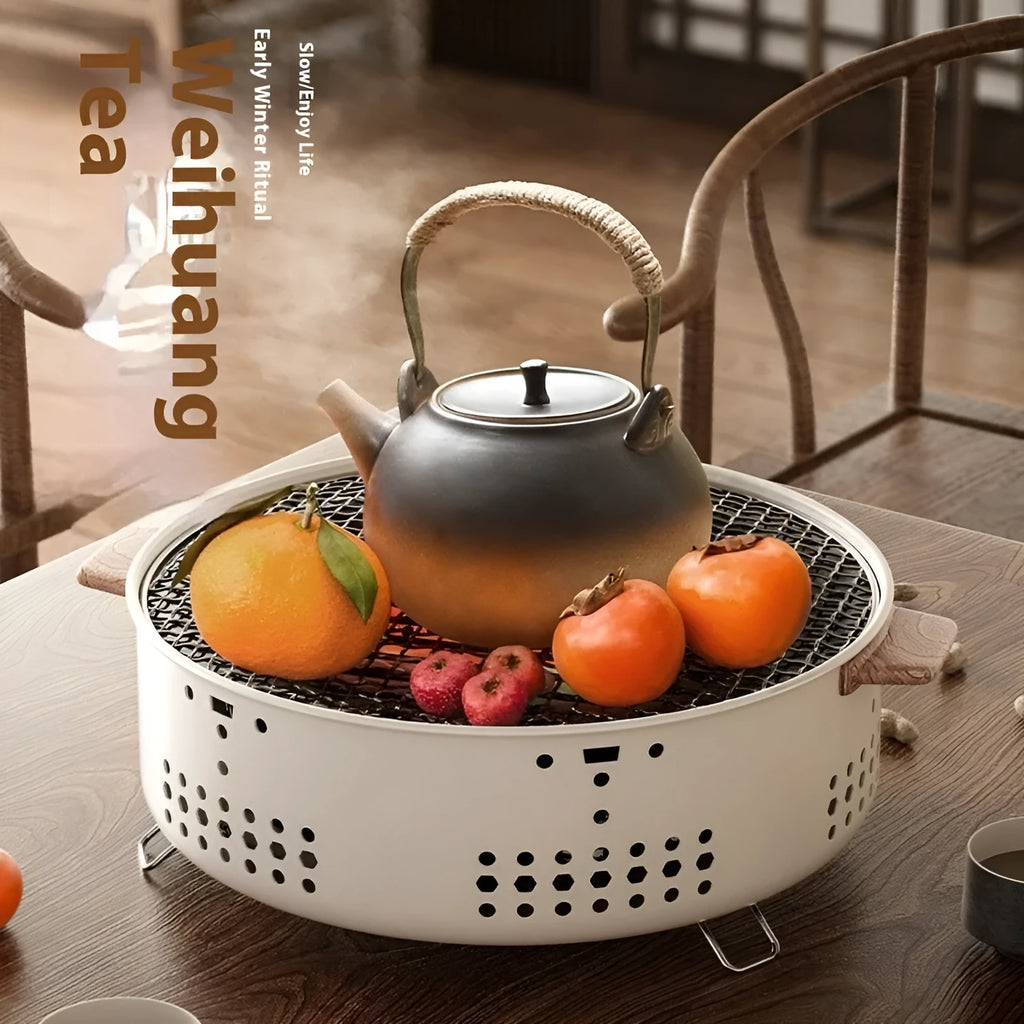 A white ceramic indoor charcoal stove with a cast iron grill rack on top, sitting on a wooden table.