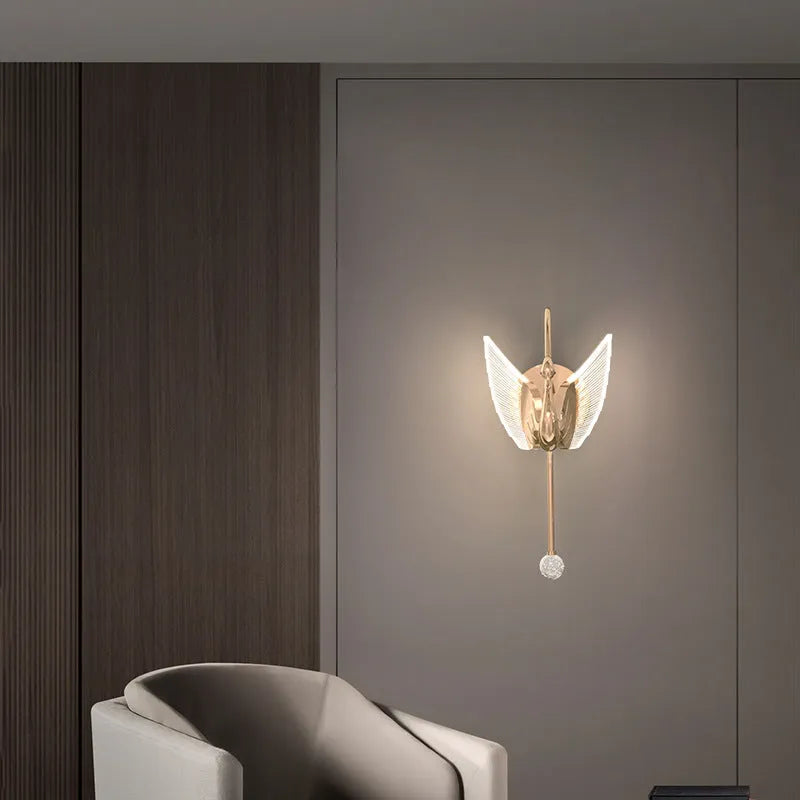 Gold modern swan-shaped wall lamp with acrylic shade mounted beside a bed.