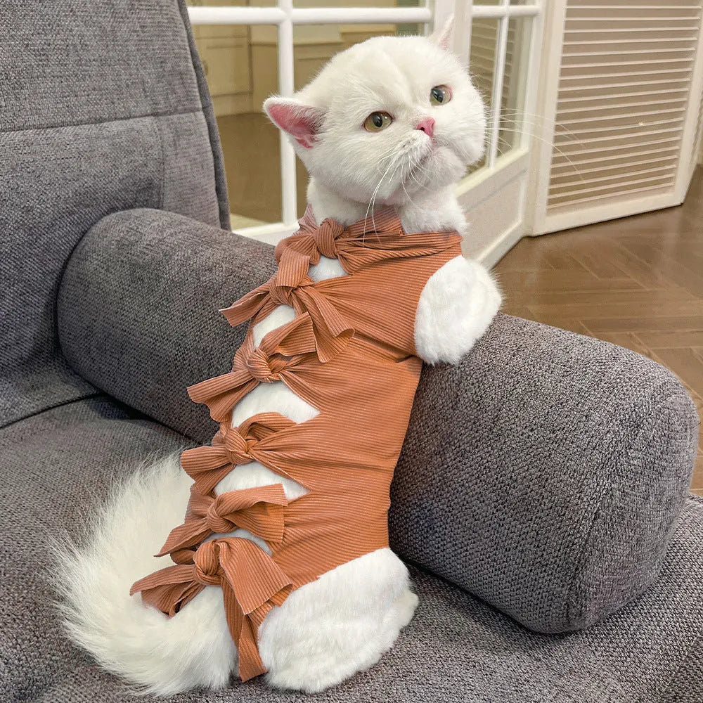A pink lace-up cat recovery suit on a grey cat, showing the back closure and full-body fit.