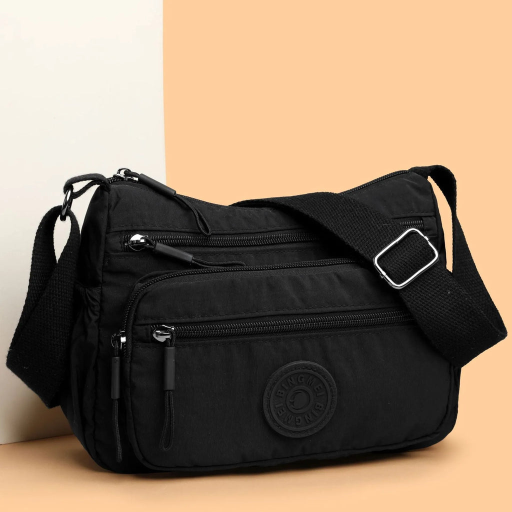 Soft water-repellent nylon crossbody bag in black with an outer pocket and zipped main compartment.