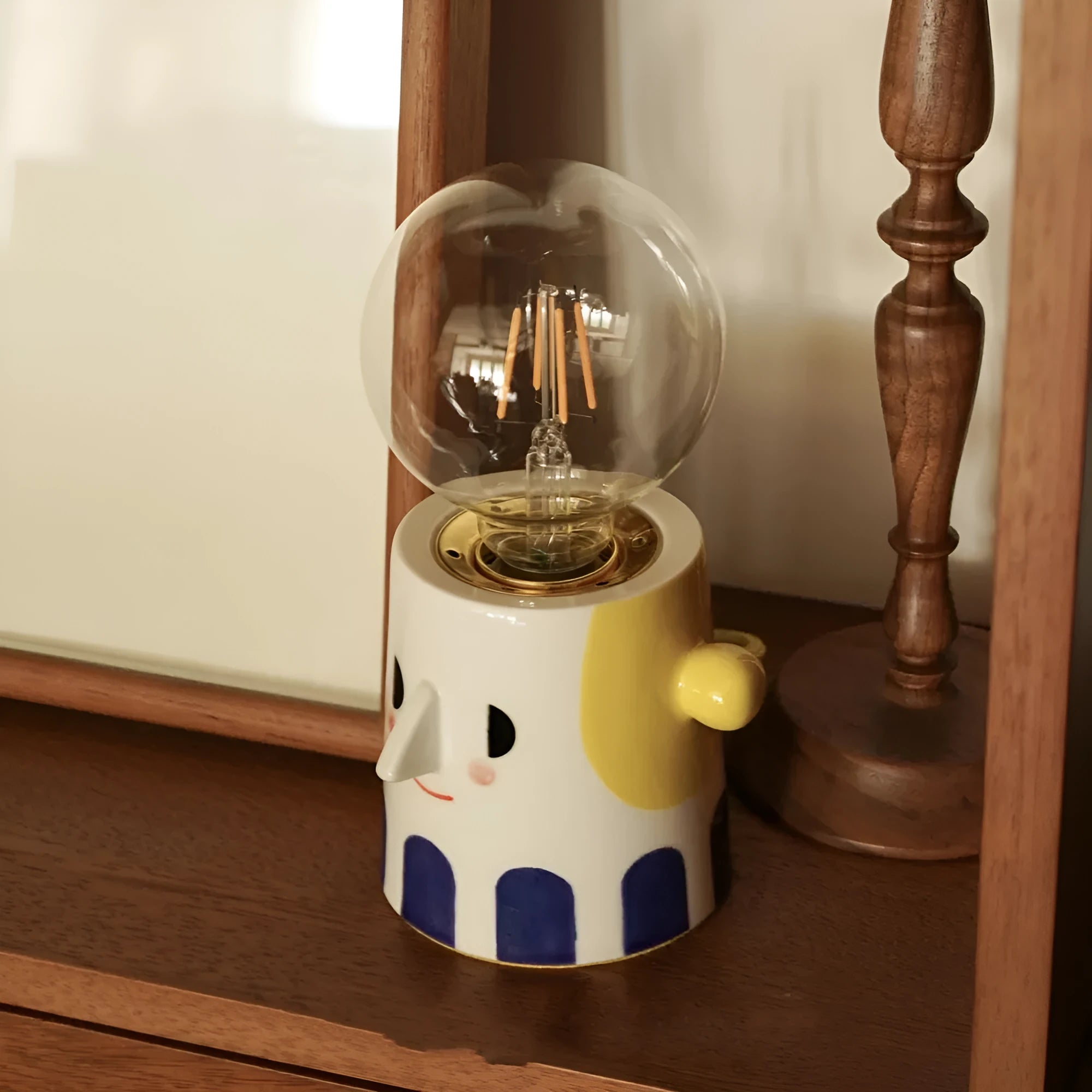 Off-white handmade ceramic table lamp with a rounded shape on a wooden surface.