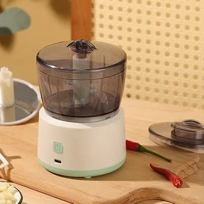 Mini electric meat grinder with transparent bowl in light green colour on a kitchen countertop.