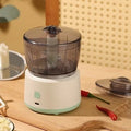 Mini electric meat grinder with transparent bowl in light green colour on a kitchen countertop.