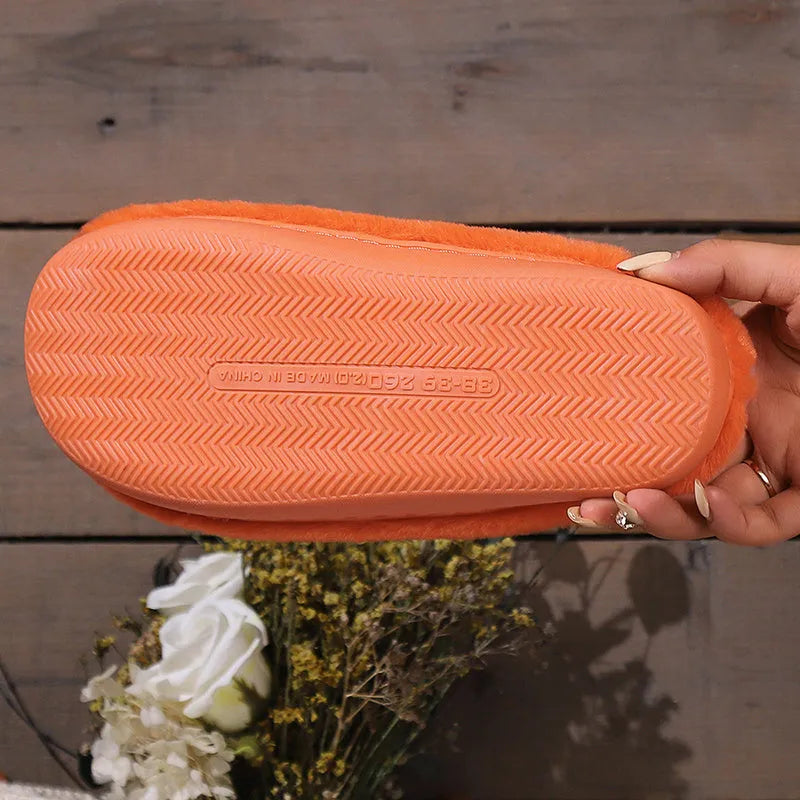 Orange Halloween pumpkin-themed plush indoor slippers with a non-slip sole on a wooden floor.