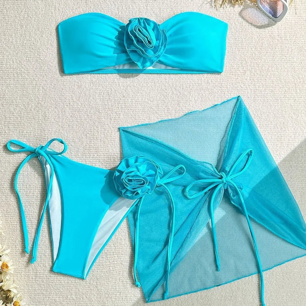 Women's pink tie-front halter swimsuit with 3D flower, high-waisted bottoms, and matching skirt laid flat.