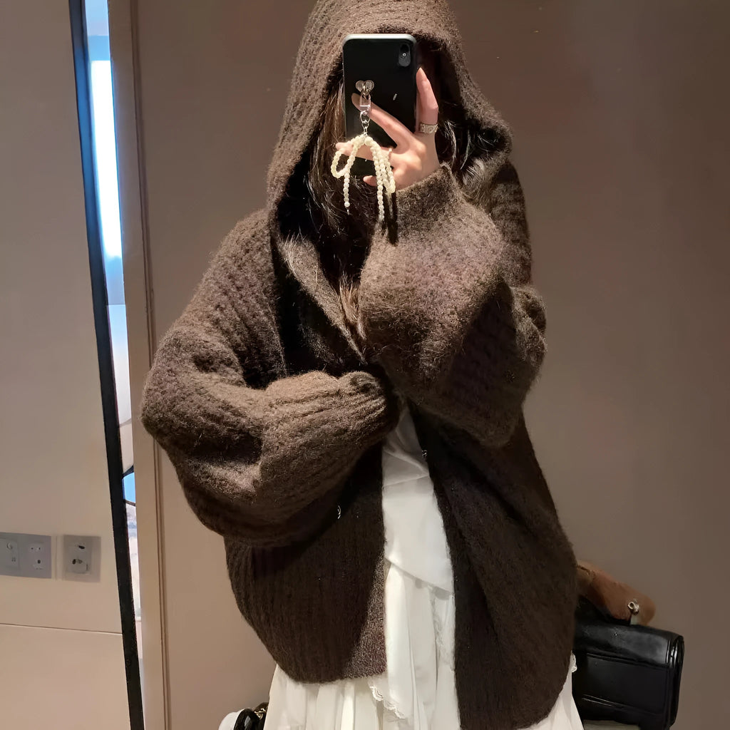 A woman wearing a loose-fit dark grey hooded cardigan made from thick acrylic blend fabric.