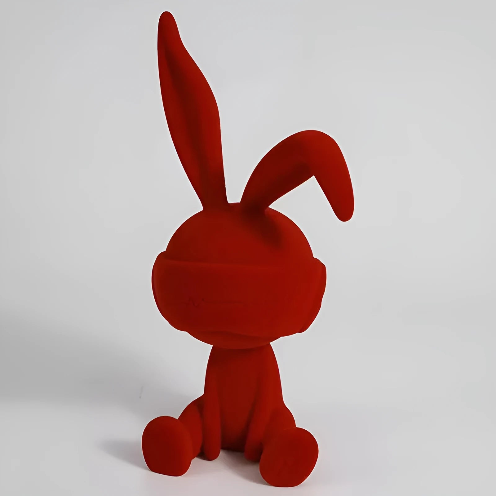 Suede blindfold rabbit resin ornament in blue, green, or red colour on a table.