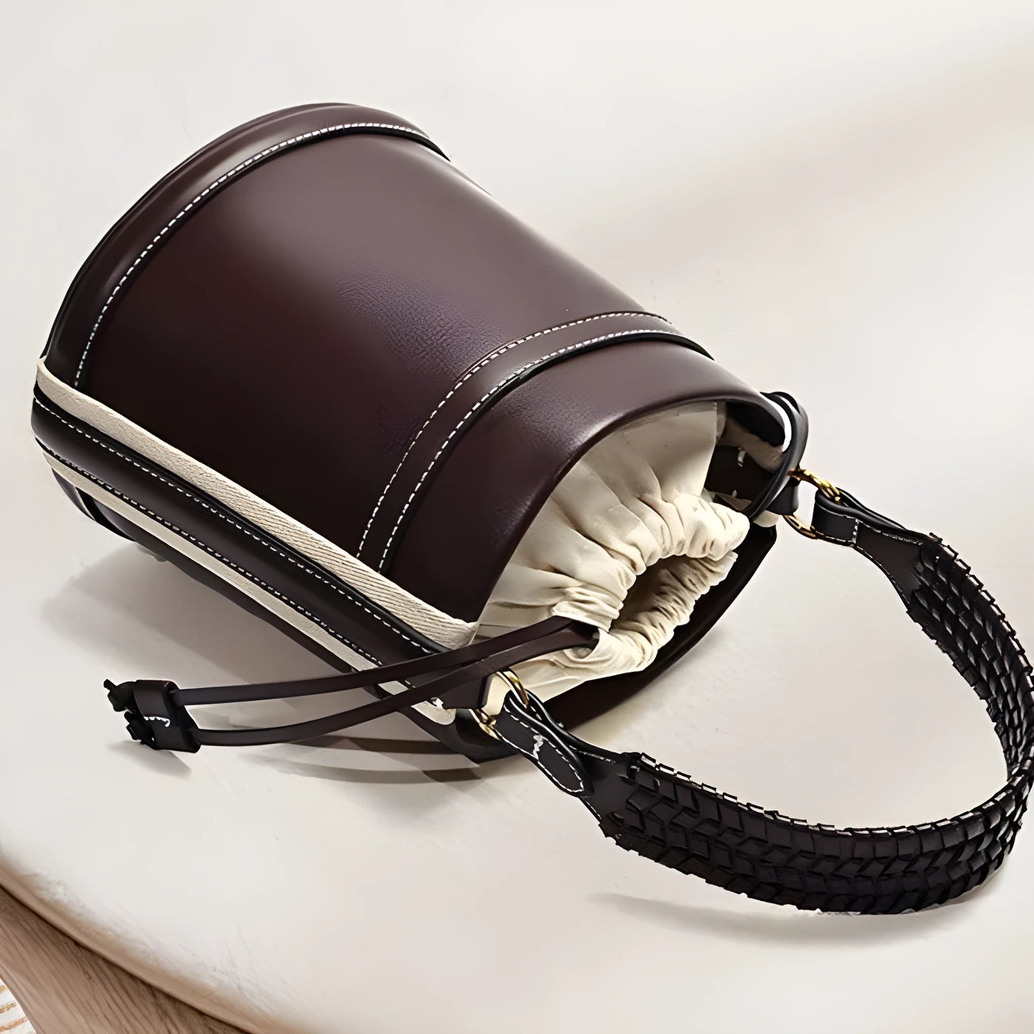 Brown PU cylindrical tote bag with dual handles, cross-body strap, and woven stitch detailing on a white background