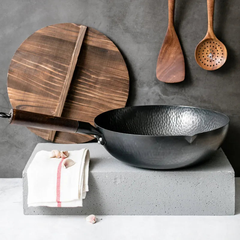 Traditional black iron wok with a long wooden handle on a kitchen counter.
