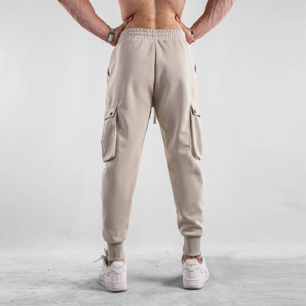 Man wearing loose-fit light grey cotton trousers with ankle ties and multiple pockets, suited for casual sports.