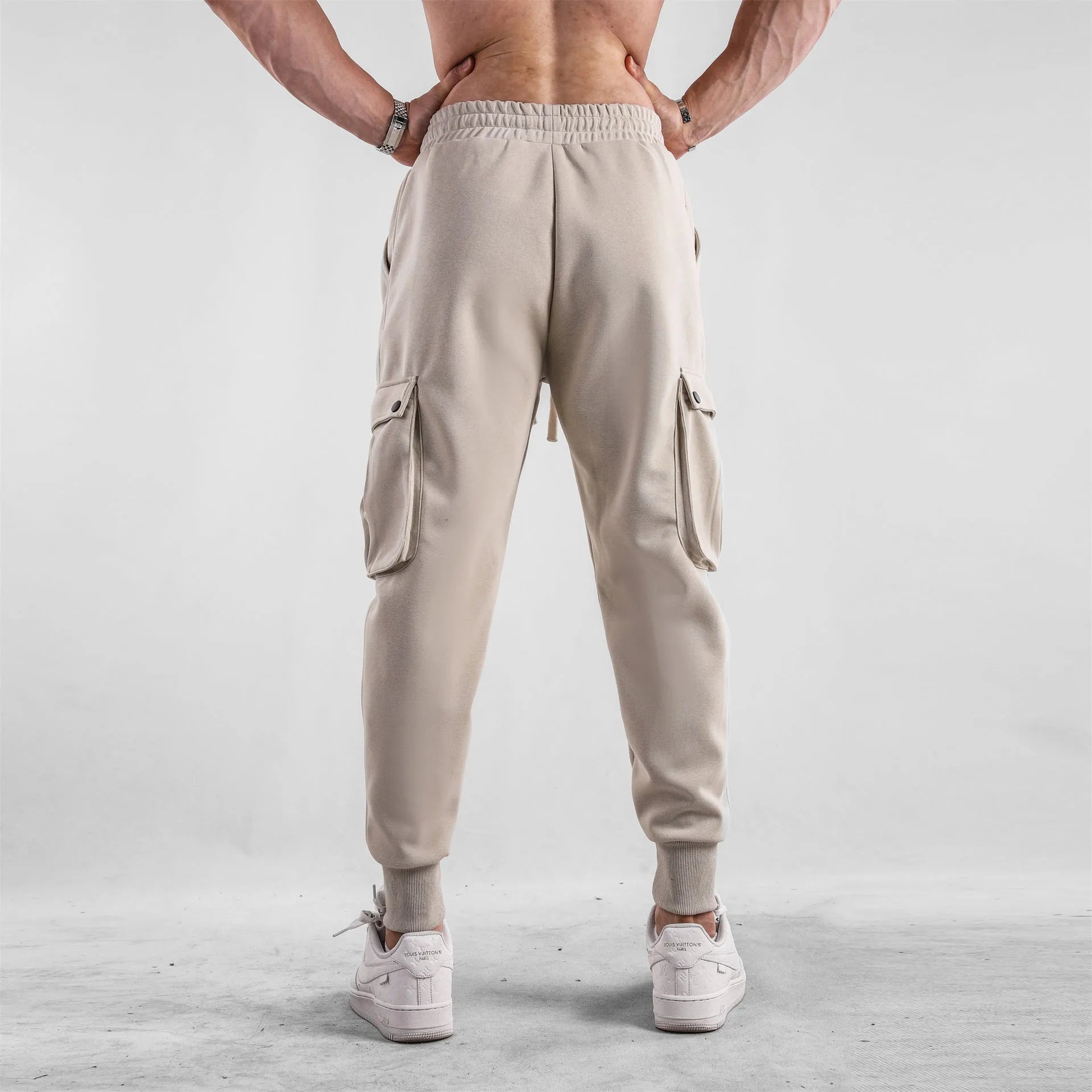 Man wearing loose-fit light grey cotton trousers with ankle ties and multiple pockets, suited for casual sports.