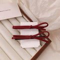 Wine red leather bow hair barrette with a metal clip on a white background