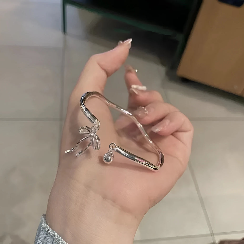 Silver tone adjustable bracelet with a 3D bow charm and magnetic clasp on a wrist.