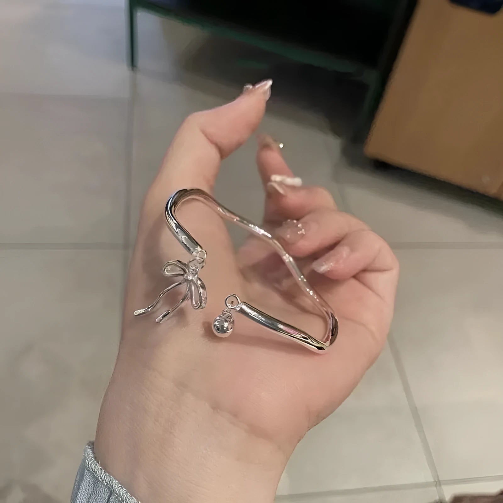 Silver tone adjustable bracelet with a 3D bow charm and magnetic clasp on a wrist.