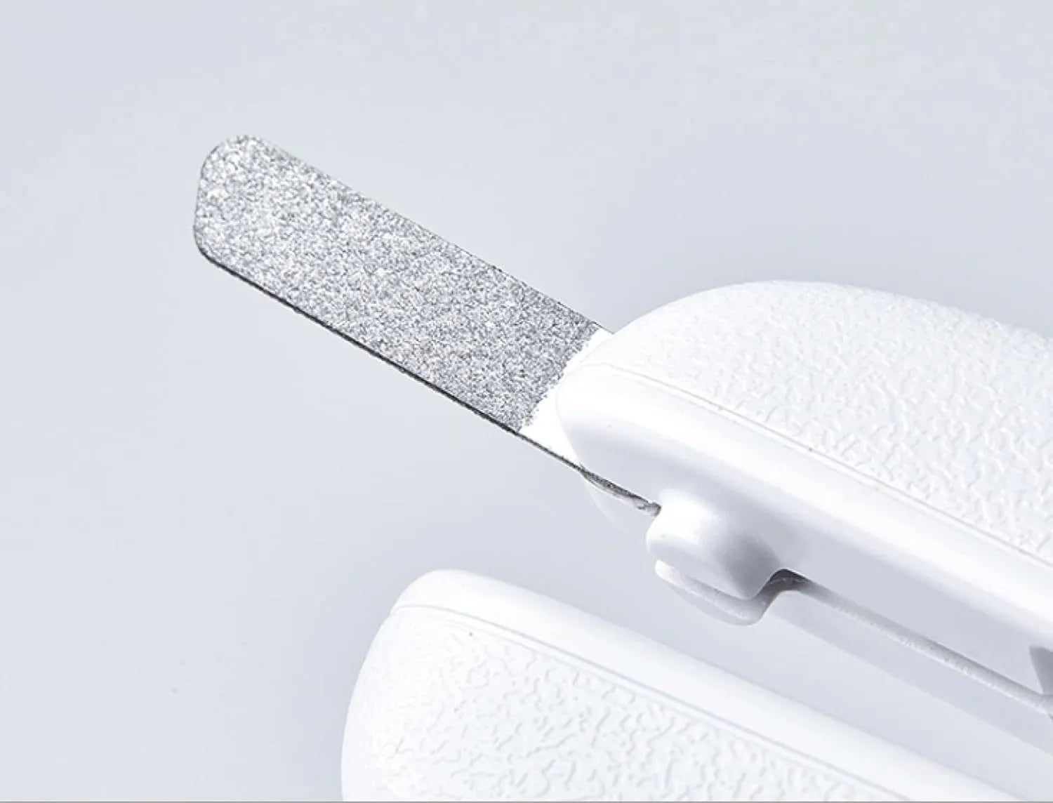 White pet nail clippers with LED light and transparent guard, shown with a separate nail file on a table.