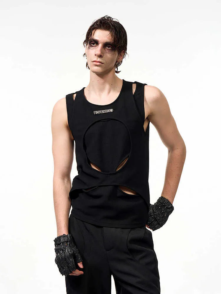 Man wearing a loose-fitting black sleeveless waistcoat with a round neck over a white t-shirt.