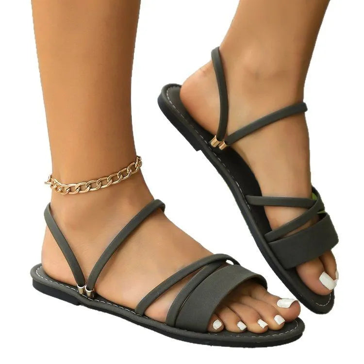 Women's flat sandals with cross strap and flip-toe buckle in black, brown, or green colours