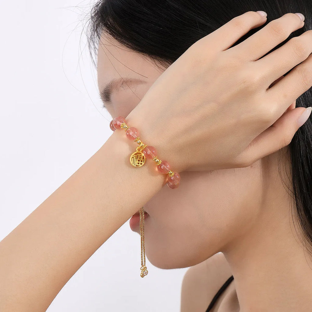 Women's strawberry quartz bracelet with a geometric fu character charm on an electroplated chain.