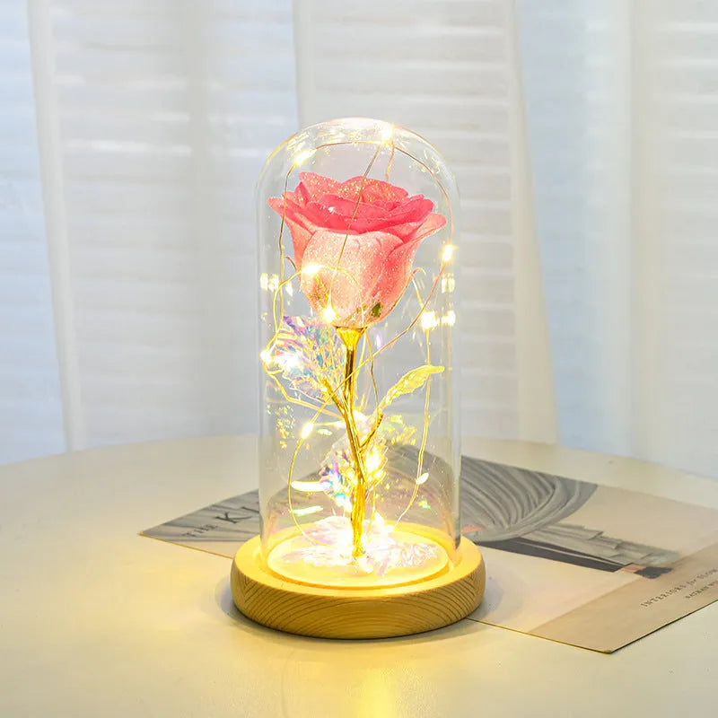 Red eternal rose with warm white LED lights under a glass dome on a table.