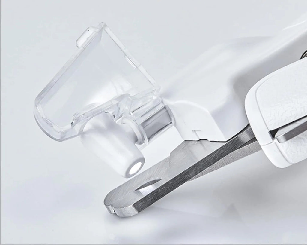 White pet nail clippers with LED light and transparent guard, shown with a separate nail file on a table.