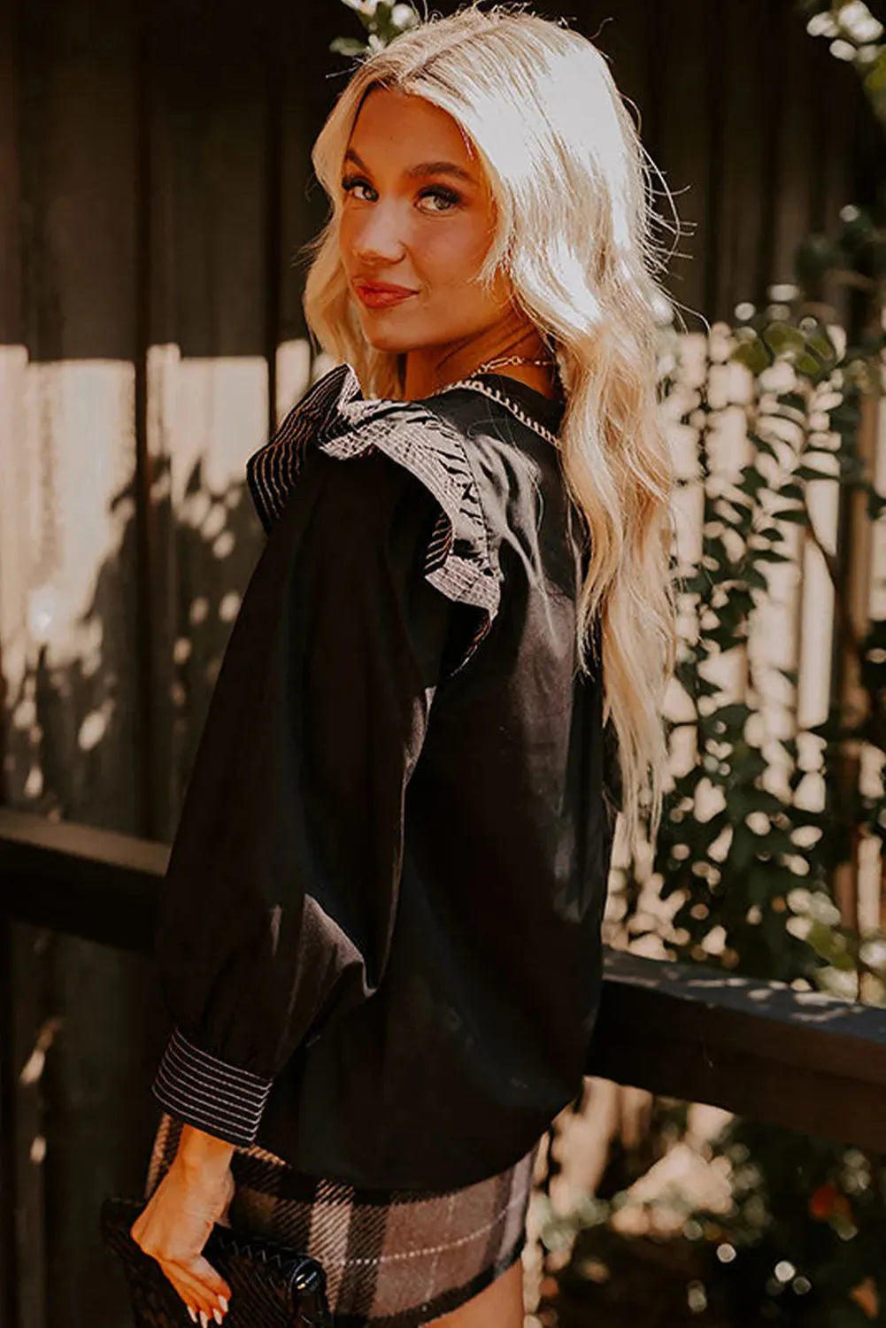 Black women's V-neck blouse with contrast stitching and long ruffle sleeves on a hanger.