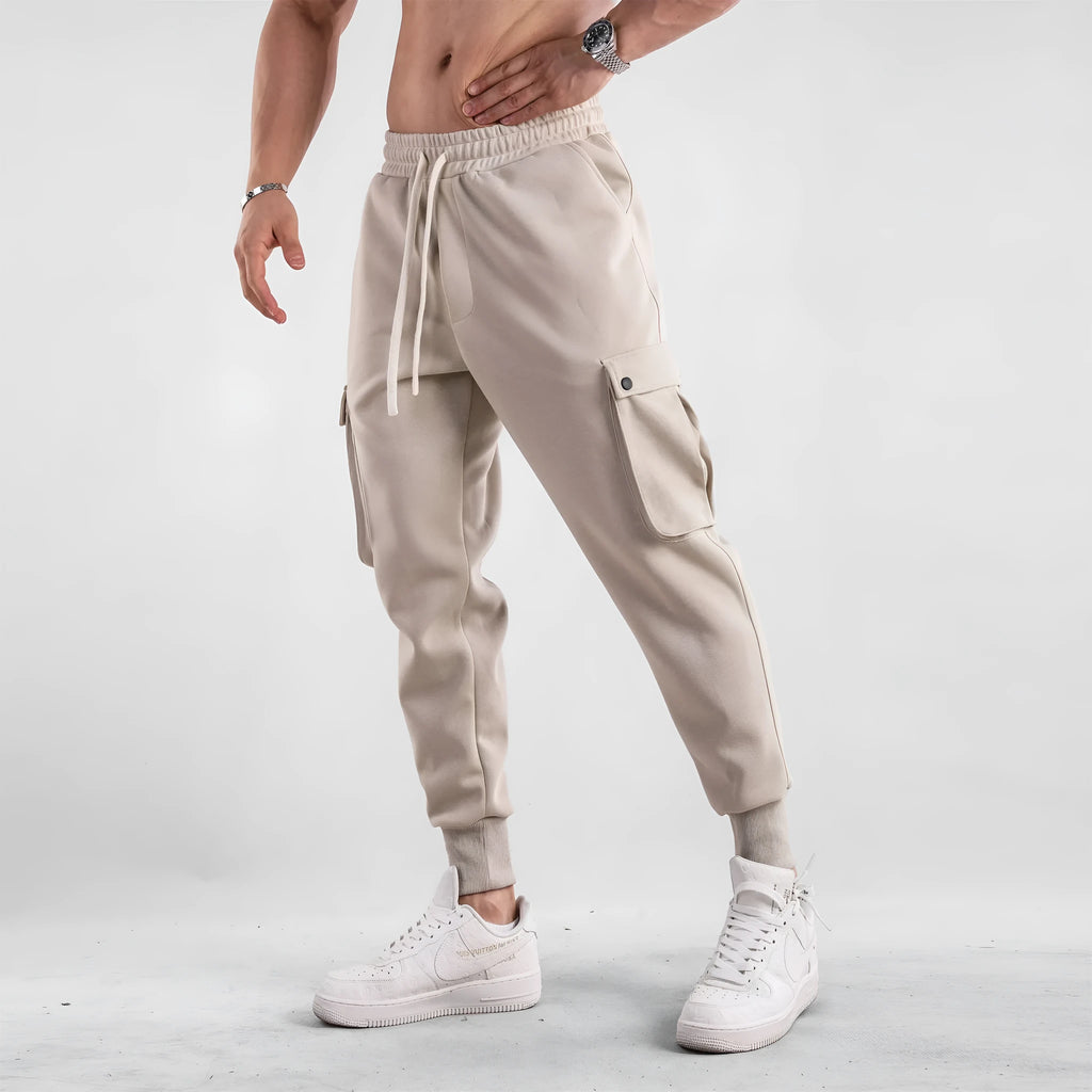Man wearing loose-fit light grey cotton trousers with ankle ties and multiple pockets, suited for casual sports.