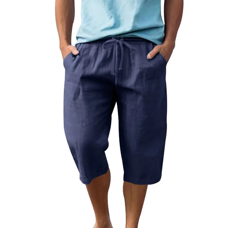 Man wearing loose-fit light khaki linen shorts with a drawstring waist and cropped leg.