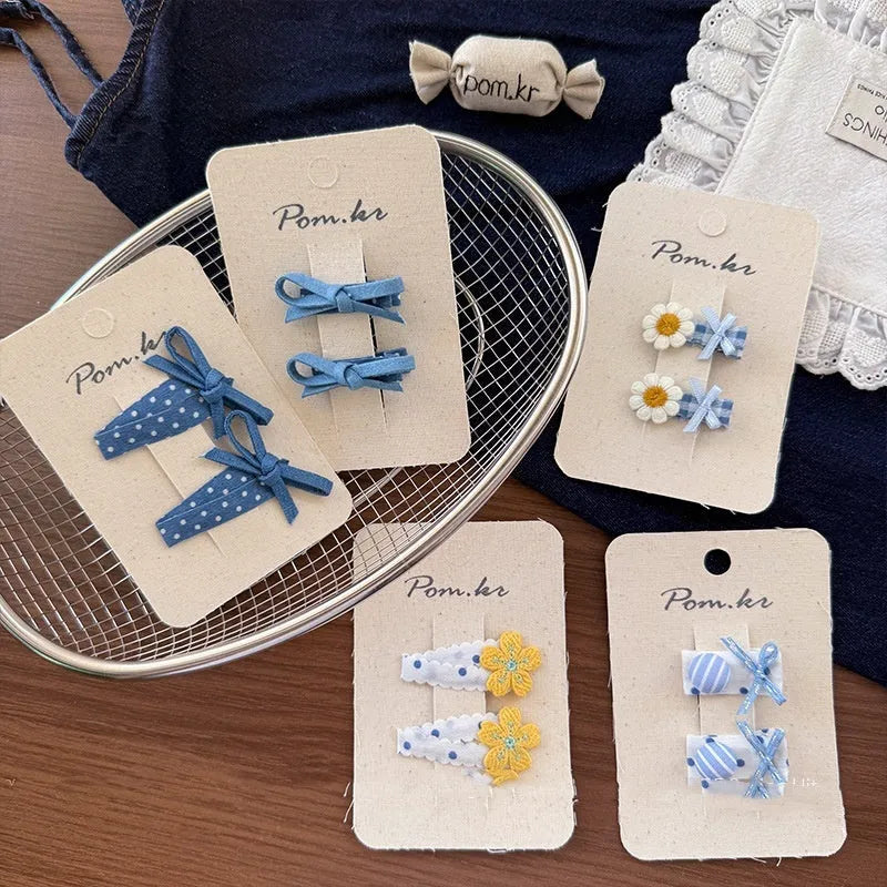 One pair of children's cloth hair clips with bow and flower detailing, shown in a choice of five styles and two clip sizes.