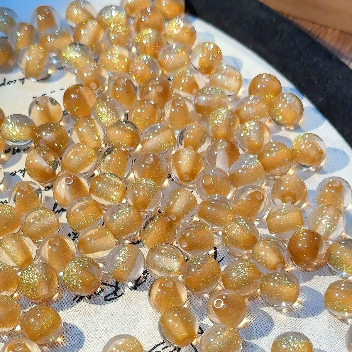 16mm round plastic scattered beads with glittering cat's eye effect in champagne colour, on a white background.