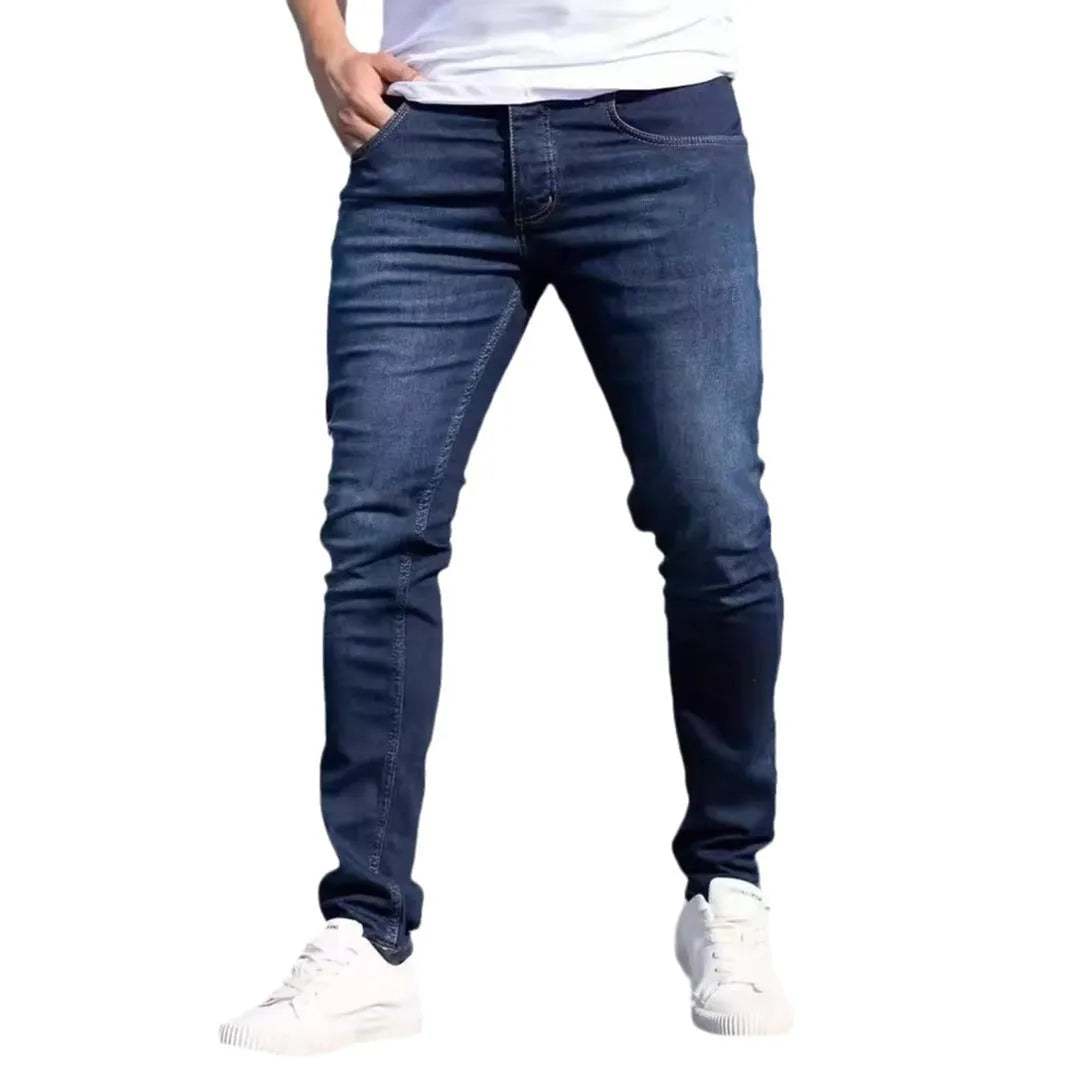 Men's dark blue skinny-fit cotton jeans with a mid-rise waist and zipper fly on a plain background.