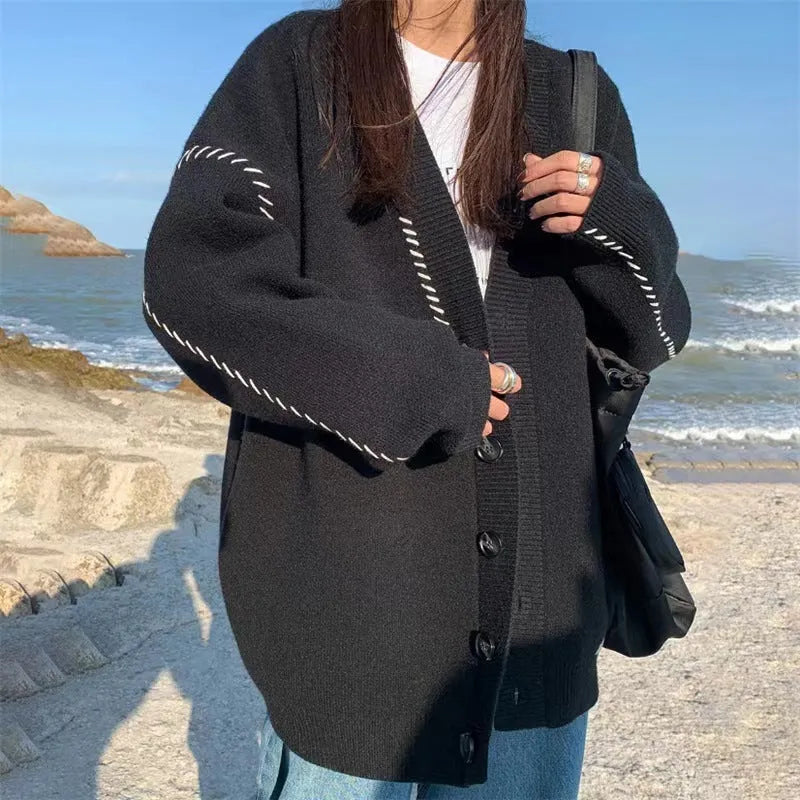 Women's loose black knitted cardigan coat with long sleeves on a hanger.