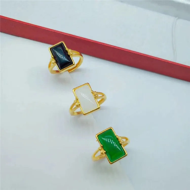 Adjustable gold-plated brass ring with a coloured gemstone inlay on a plain background.
