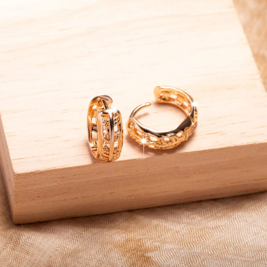 Close-up of rose gold plated copper stud earrings with hollow leaf and heart shapes on a grey background.