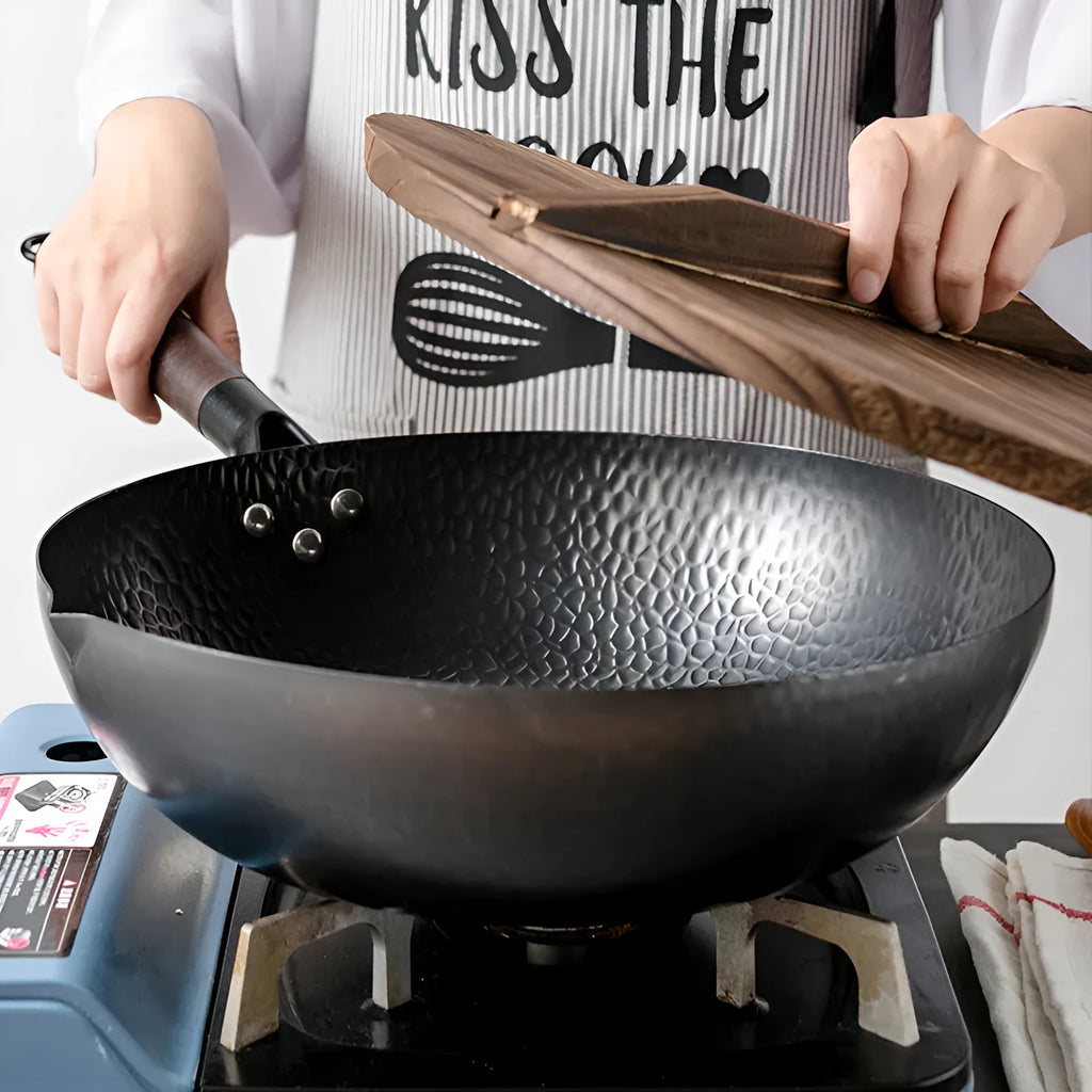 Traditional black iron wok with a long wooden handle on a kitchen counter.