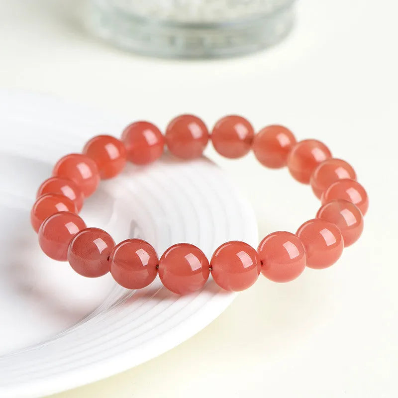 Natural cherry red agate beaded bracelet with adjustable metal clasp on a wrist, showing scattered polished stones.