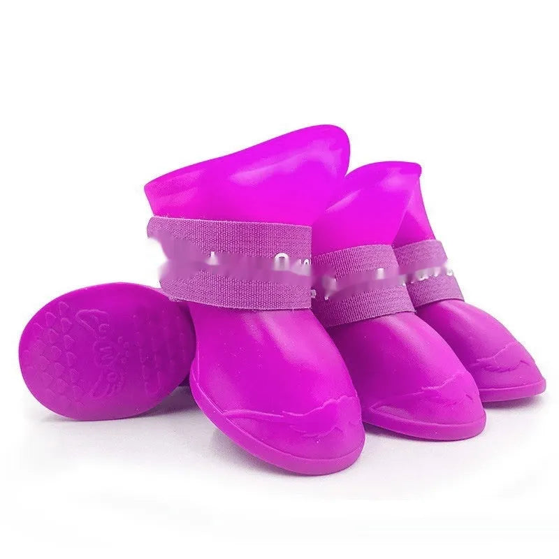 Set of four soft-soled rubber rain shoes for dogs in various colours on a wet surface.