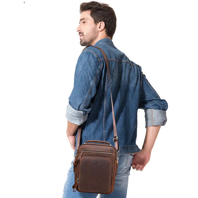Men's brown Crazy Horse leather crossbody bag with sewing line detail on a table.