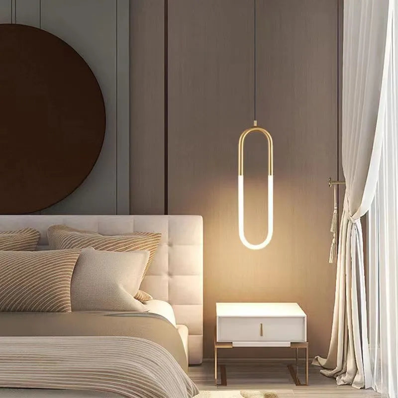 Minimalist black U-shaped pendant light with a downward-facing bulb mounted next to a bed.