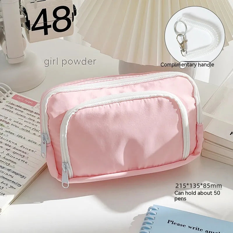 Double layer pencil case in pink with a gift handle, shown next to pens and pencils.