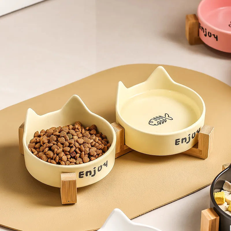 Porcelain cat bowl in a wooden anti-tip frame, showing cat's paw print design in pink.
